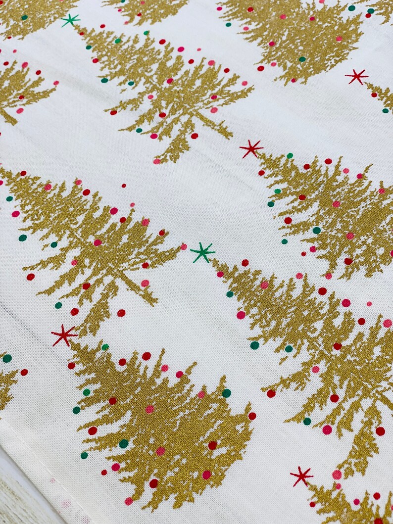 May include: White fabric with a gold glitter Christmas tree pattern. The trees are decorated with red and green glitter ornaments.