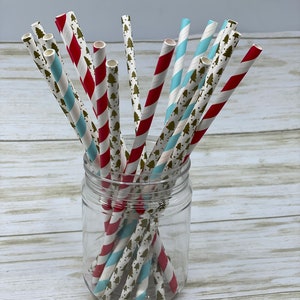 May include: A glass jar filled with red and blue striped paper straws with a gold tree pattern. The straws are arranged in a criss-cross pattern.