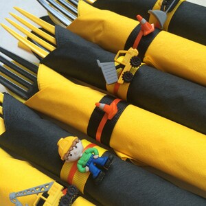 May include: Yellow and black construction themed napkin rings with a variety of construction vehicles and a construction worker figurine.