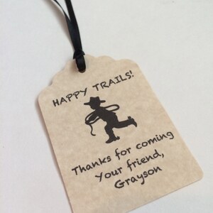 May include: A brown paper gift tag with a black silhouette of a cowboy riding a horse. The tag says "Happy Trails!" and "Thanks for coming your friend, Grayson".