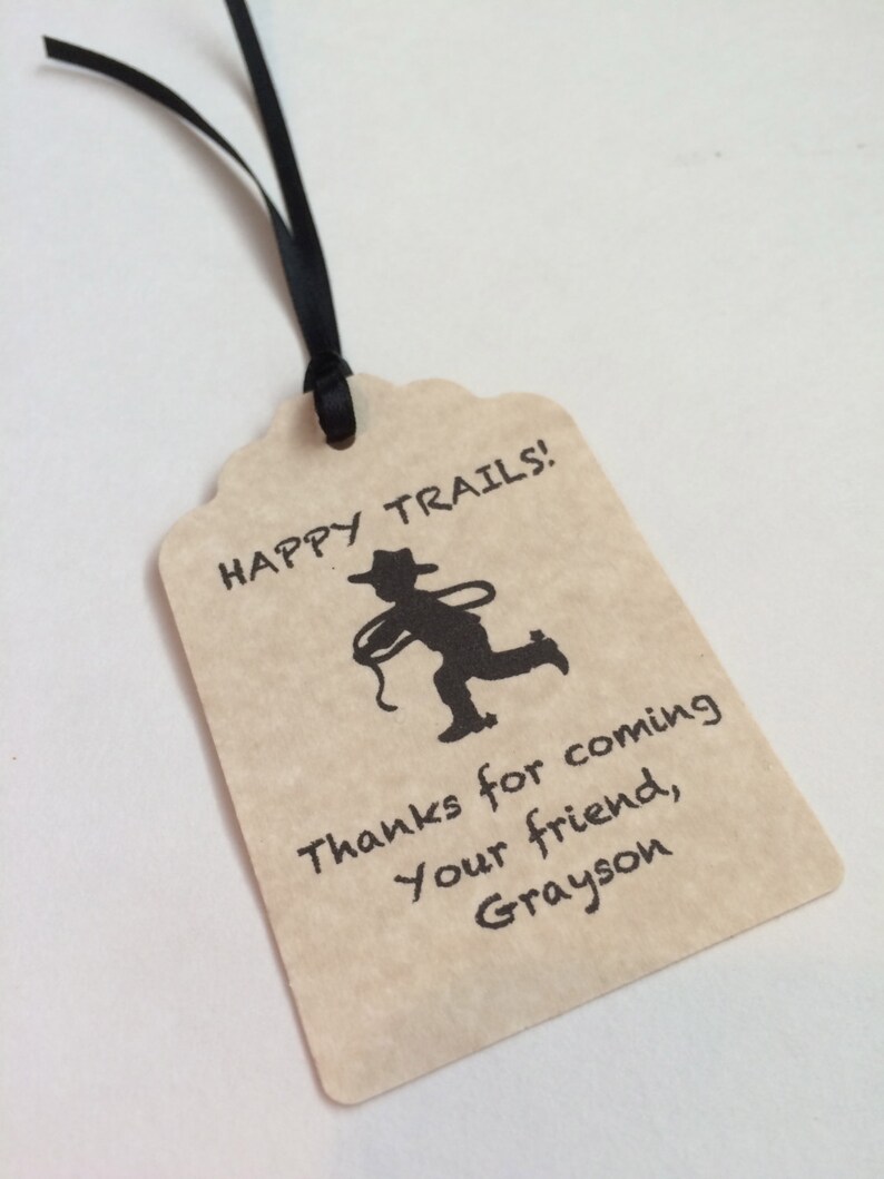 May include: A brown paper gift tag with a black silhouette of a cowboy riding a horse. The tag says "Happy Trails!" and "Thanks for coming your friend, Grayson".