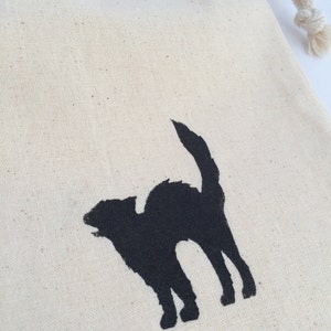 K&ouml;nnte beinhalten: Eine wei&szlig;e Baumwolltasche mit Kordelzug, auf der eine schwarze Silhouette einer Katze aufgedruckt ist.