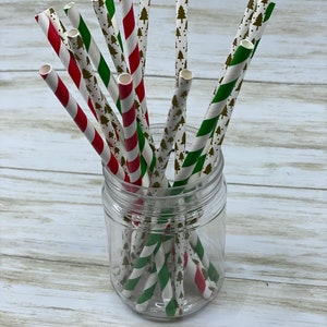 May include: A glass jar filled with red and green striped paper straws with a white background and a gold Christmas tree pattern.