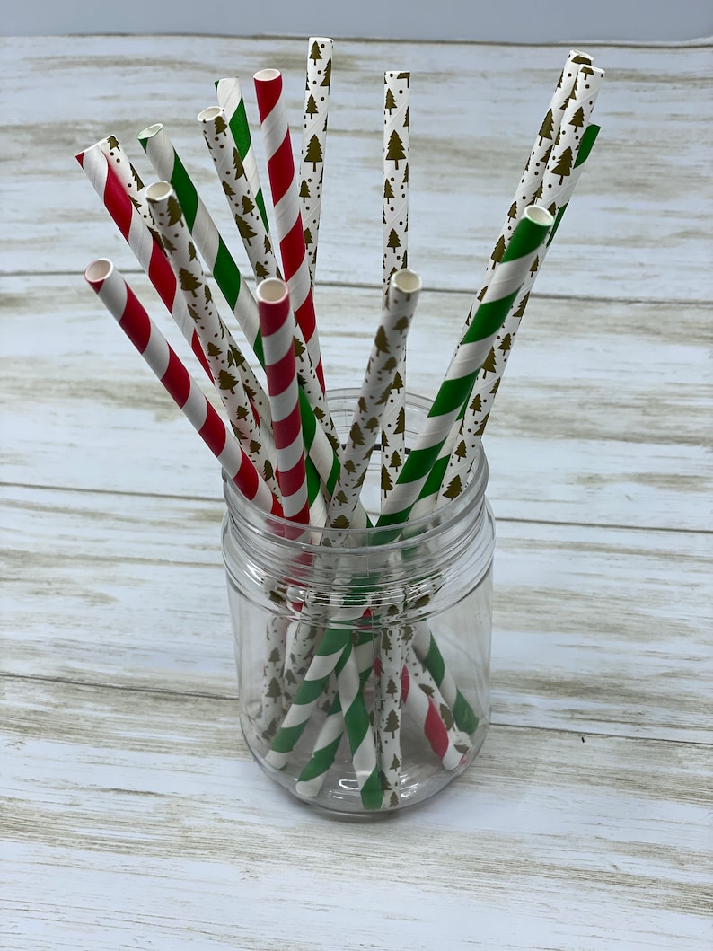 May include: A glass jar filled with red and green striped paper straws with a white background and a gold Christmas tree pattern.