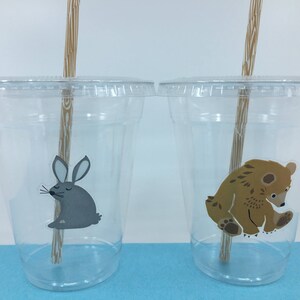 May include: Two clear plastic cups with straws and animal stickers. The cup on the left has a gray rabbit sticker and the cup on the right has a brown bear sticker.