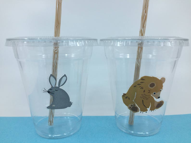 May include: Two clear plastic cups with straws and animal stickers. The cup on the left has a gray rabbit sticker and the cup on the right has a brown bear sticker.
