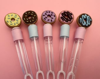 May include: Six clear plastic bubble wands with donut-shaped tops. The donuts are decorated with different colored icings and sprinkles. The wands are pink, blue, and purple.