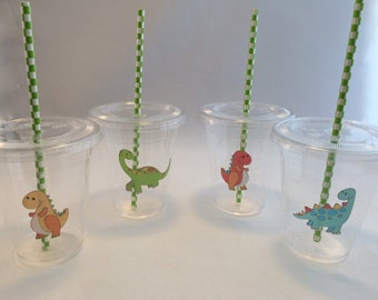 May include: Four clear plastic cups with green and white striped straws. Each cup has a different dinosaur sticker on the front. The dinosaurs are green, red, orange, and blue.