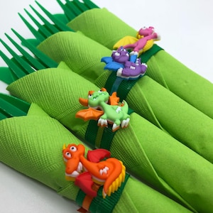 May include: Four green napkins with plastic forks wrapped inside. Each napkin is secured with a colourful plastic dinosaur ring.
