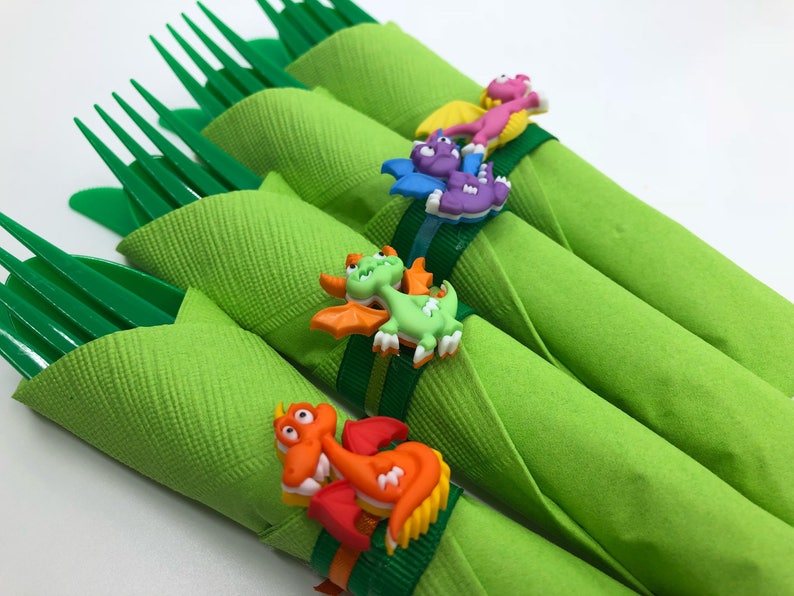 May include: Four green napkins with plastic forks wrapped inside. Each napkin is secured with a colourful plastic dinosaur ring.