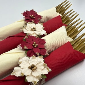 May include: Four gold forks wrapped in white and red napkins with red and white poinsettia paper flowers.