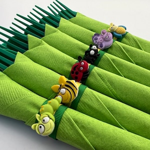 May include: Green napkins with colorful bug-themed napkin rings. The rings feature a ladybug, a bee, a caterpillar, a spider, a butterfly, and a dragonfly.