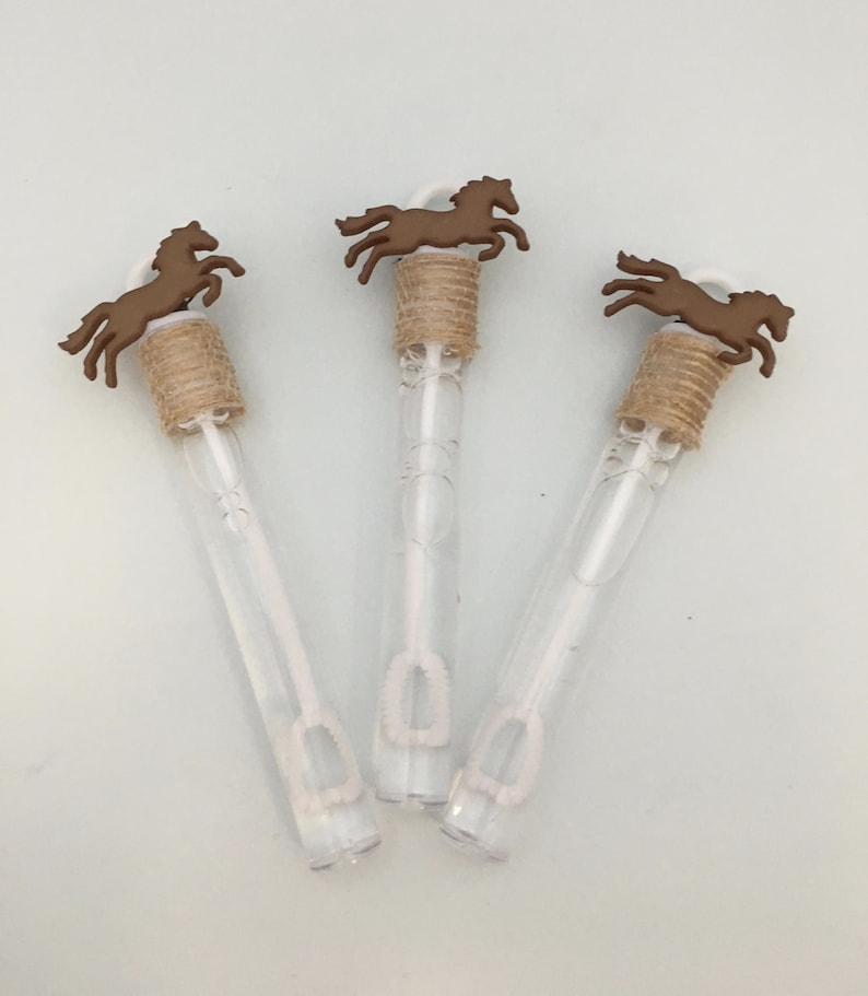 Puede incluir: Tres varitas de burbujas de pl&aacute;stico transparente con recortes de caballos marrones y cinta de arpillera marr&oacute;n en la parte superior. Las varitas est&aacute;n llenas de soluci&oacute;n de burbujas.