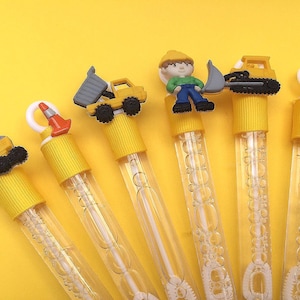 May include: Six clear plastic bubble wands with yellow caps, each topped with a construction-themed figure including a crane, a traffic cone, a dump truck, a worker in a hard hat, an excavator, and another traffic cone, all filled with bubble solution.