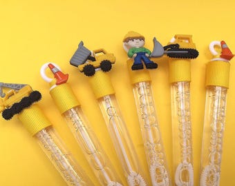 May include: Six clear plastic bubble wands with yellow caps, each topped with a construction-themed figure including a crane, a traffic cone, a dump truck, a worker in a hard hat, an excavator, and another traffic cone, all filled with bubble solution.