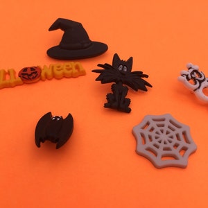 May include: A set of six Halloween-themed buttons featuring a witch's hat, a black cat, a bat, a spiderweb, a pumpkin, and the word "Halloween".