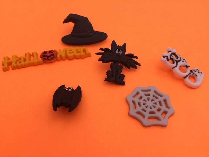 May include: A set of six Halloween-themed buttons featuring a witch's hat, a black cat, a bat, a spiderweb, a pumpkin, and the word "Halloween".