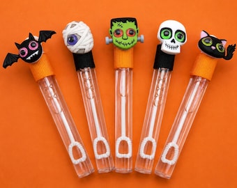 Puede incluir: Cinco varitas de burbujas de plástico transparente con adornos temáticos de Halloween. Los adornos incluyen un murciélago negro, una momia blanca, un monstruo de Frankenstein verde, una calavera blanca y un gato negro con tapa de color.
