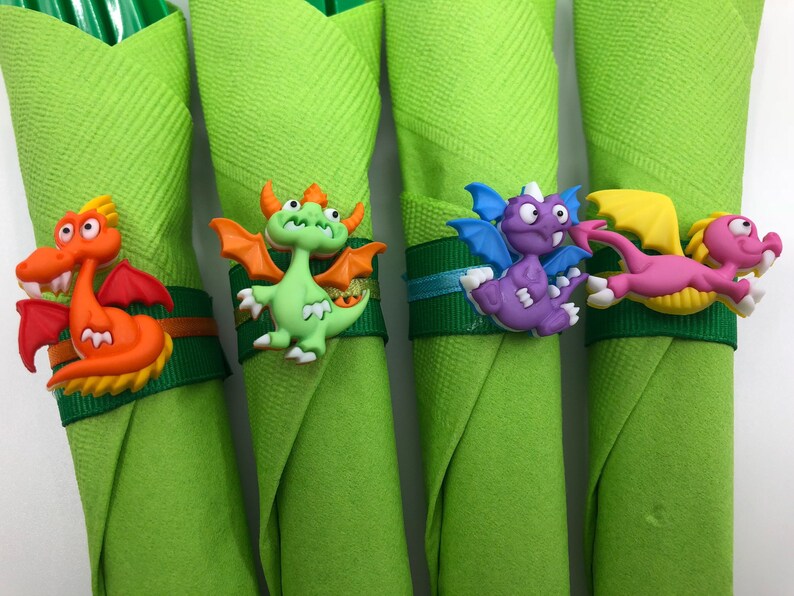 May include: Four green napkins with dragon-shaped napkin rings. The dragons are orange, green, purple, and pink.