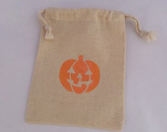 May include: A small, beige, drawstring bag with a pumpkin face printed on the front. The pumpkin is orange with a black outline.