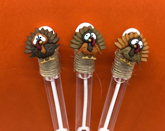 Puede incluir: Tres tubos de plástico transparente con cuerda marrón envuelta alrededor de la parte superior. Cada tubo tiene una pequeña figura de pavo marrón, naranja y rojo unida a la parte superior.