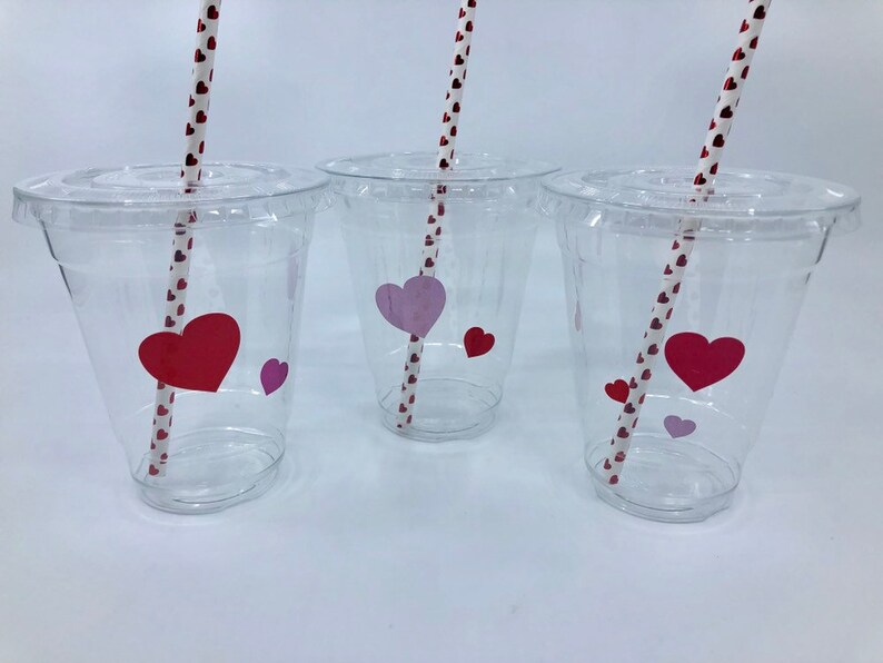 May include: Three clear plastic cups with red and pink heart stickers and red and white striped straws.
