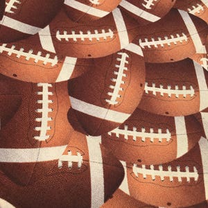 May include: A close-up of a fabric with a repeating pattern of brown and white footballs. The footballs have white laces and are arranged in a staggered pattern.