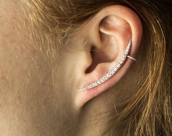 Puede incluir: Primer plano de la oreja de una persona con un pendiente de aro de plata adornado con pequeños cristales transparentes. El pendiente de aro es curvo y se extiende desde el lóbulo de la oreja hasta la parte superior de la oreja.