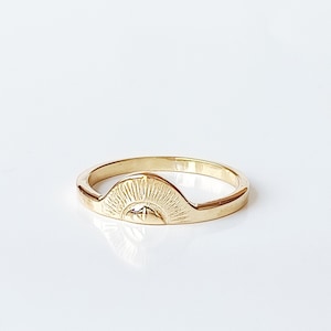 May include: A gold ring with a sun design. The sun has a face and rays coming out from it.
