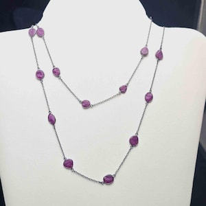 May include: Two layered necklace with oval-shaped, deep pink gemstones set along a delicate silver chain. The gemstones are evenly spaced, creating a sophisticated and elegant design. The necklace is displayed on a white mannequin.