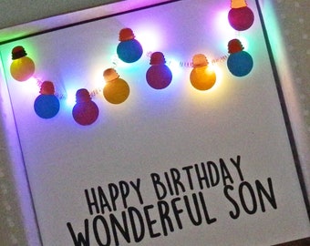 May include: A white card with a string of colorful lightbulbs and the text "Happy Birthday Wonderful Son".