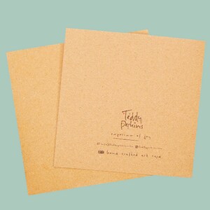 May include: A brown card with the text "Teddy Perkins, emporium of joy" and "hand crafted art cards" printed on it.