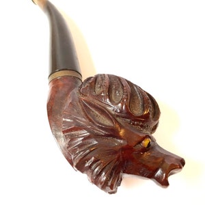 Puede incluir: Una pipa de madera tallada en forma de cabeza de lobo. La pipa tiene un tinte marr&oacute;n y una boquilla negra.
