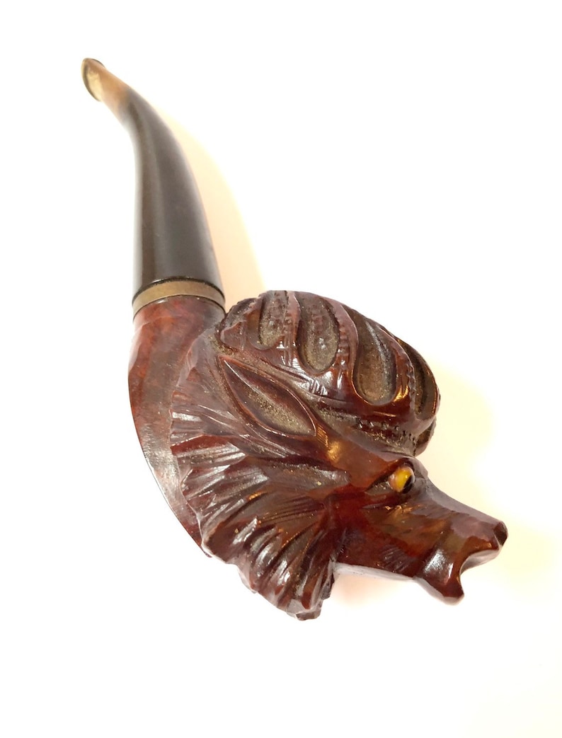 Puede incluir: Una pipa de madera tallada en forma de cabeza de lobo. La pipa tiene un tinte marr&oacute;n y una boquilla negra.