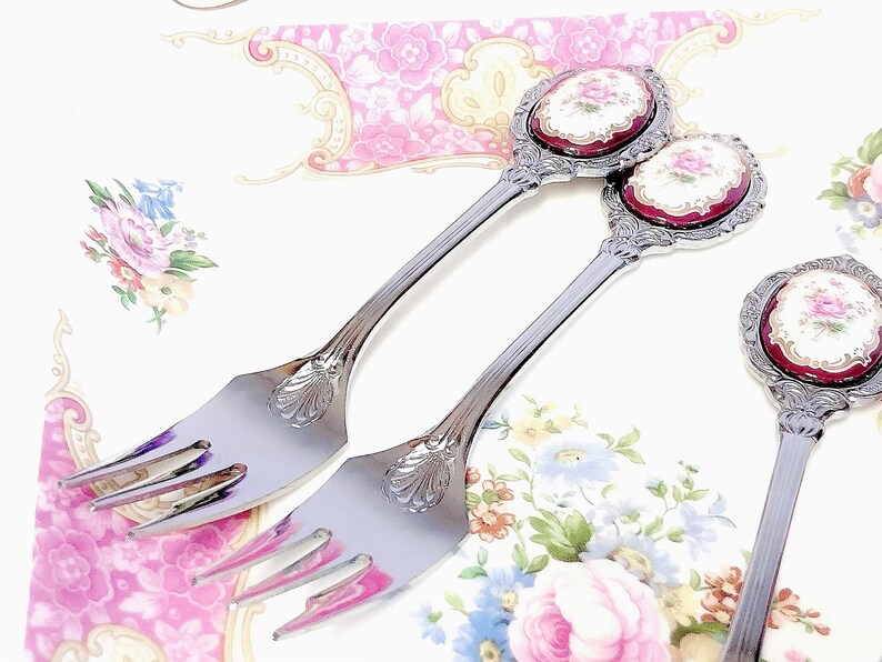 Pu&ograve; includere: Tre forchette d'argento con manici decorati con motivi floreali in tonalit&agrave; di rosso, bianco e oro. I manici sono sormontati da medaglioni ovali in porcellana con motivi floreali.