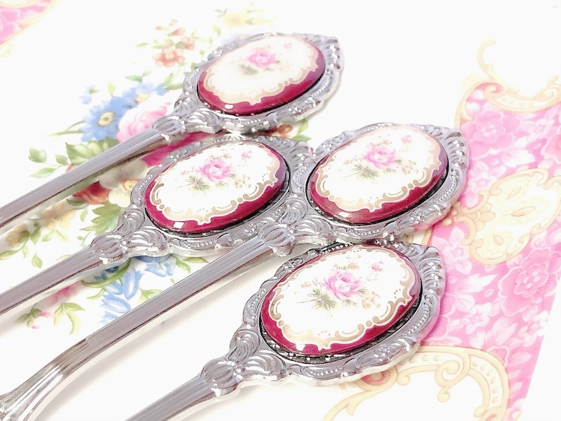 Pu&ograve; includere: Set di tre cucchiaini d'argento con manici decorati e disegni floreali rossi e bianchi sulla parte superiore di ogni manico.