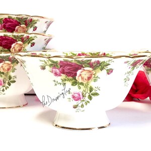 May include: Set of four white ceramic bowls with a gold rim and a floral pattern featuring red, pink, and yellow roses. The bowls have a scalloped edge and a pedestal base.