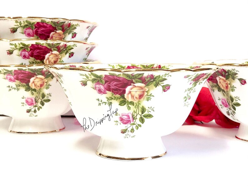 May include: Set of four white ceramic bowls with a gold rim and a floral pattern featuring red, pink, and yellow roses. The bowls have a scalloped edge and a pedestal base.