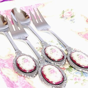 Pu&ograve; includere: Set di quattro cucchiai e forchette argentate con manici decorati. Ogni manico presenta un cammeo in porcellana rossa e bianca con un motivo floreale.