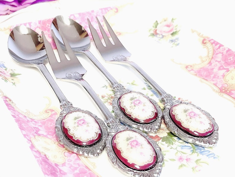 Pu&ograve; includere: Set di quattro cucchiai e forchette argentate con manici decorati. Ogni manico presenta un cammeo in porcellana rossa e bianca con un motivo floreale.