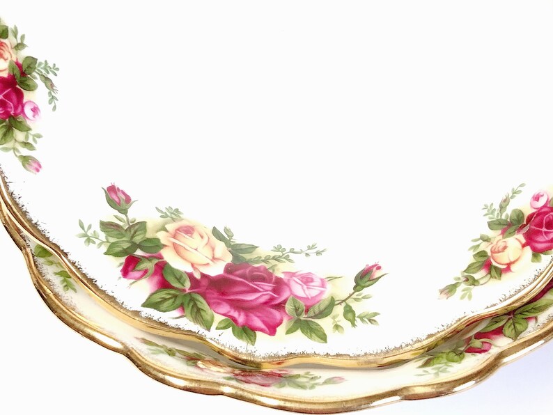 May include: Two white ceramic plates with a gold rim and a floral design featuring red, yellow, and green roses. The plates are stacked on top of each other.
