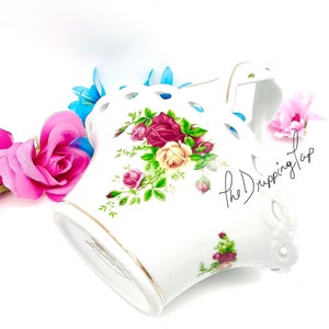 May include: White porcelain basket with a lace design and floral pattern. The basket features a handle and is decorated with red, yellow, and pink roses.