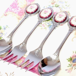 Pu&ograve; includere: Set di quattro cucchiai e forchette d'argento con manici decorati. Ogni manico presenta un cammeo in porcellana rossa e bianca con un motivo floreale.