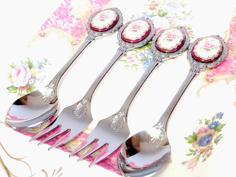 Pu&ograve; includere: Set di quattro cucchiai e forchette d'argento con manici decorati. Ogni manico presenta un cammeo in porcellana rossa e bianca con un motivo floreale.