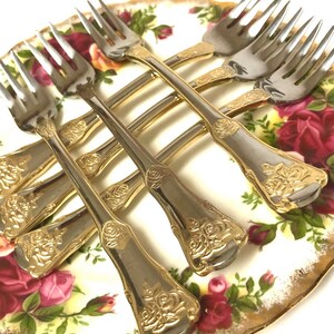 May include: Set of six gold-plated forks with rose design on a white plate with red roses.