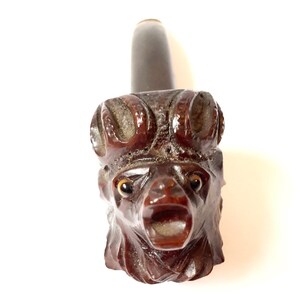 Puede incluir: Una pipa de madera marr&oacute;n oscuro tallada en forma de cabeza de animal con ojos grandes y boca abierta. La pipa es una pipa de fumar tradicional.