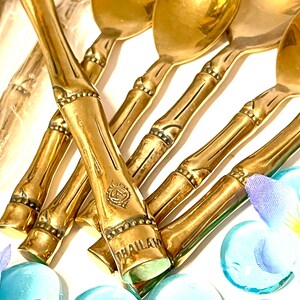 Puede incluir: Un juego de cucharas de bamb&uacute; doradas con un dise&ntilde;o decorativo. Las cucharas tienen un borde con cuentas y la palabra "THAILAND" est&aacute; grabada en el mango.