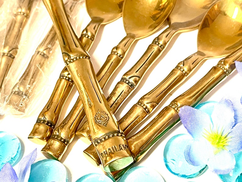 Puede incluir: Un juego de cucharas de bamb&uacute; doradas con un dise&ntilde;o decorativo. Las cucharas tienen un borde con cuentas y la palabra "THAILAND" est&aacute; grabada en el mango.