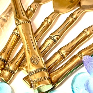 Puede incluir: Un juego de cucharas de estilo bamb&uacute; doradas con un dise&ntilde;o decorativo y la palabra "THAILAND" grabada en el mango.