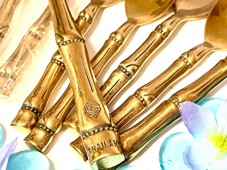 Puede incluir: Un juego de cucharas de estilo bamb&uacute; doradas con un dise&ntilde;o decorativo y la palabra "THAILAND" grabada en el mango.